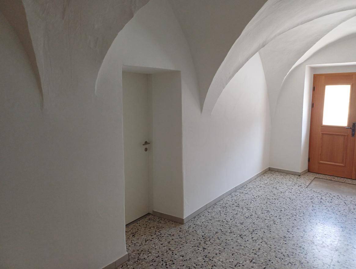 Detailansicht eines Flurs mit gewölbter Decke, Terrazzoboden und einer Holztür, die den Eingangsbereich bildet.