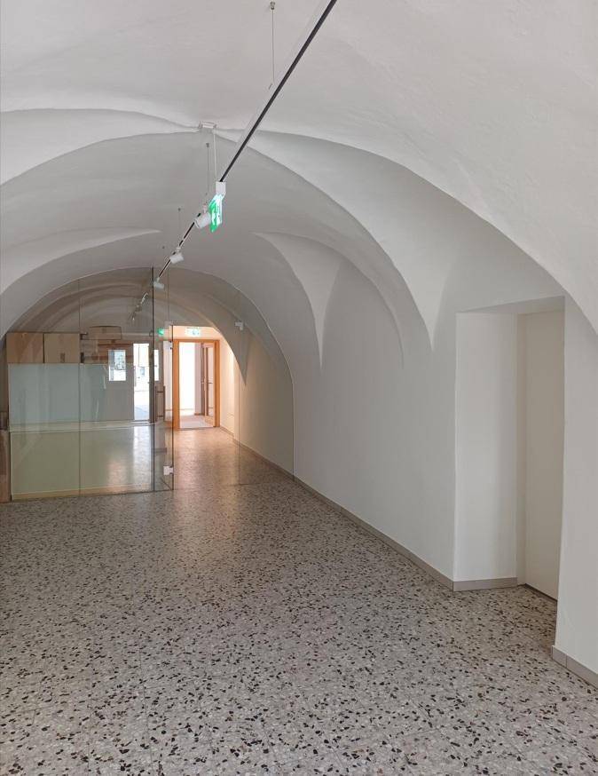 Geräumiger Flur mit gewölbter Decke, Terrazzoboden und einer modernen Glastrennwand, die den Raum unterteilt.