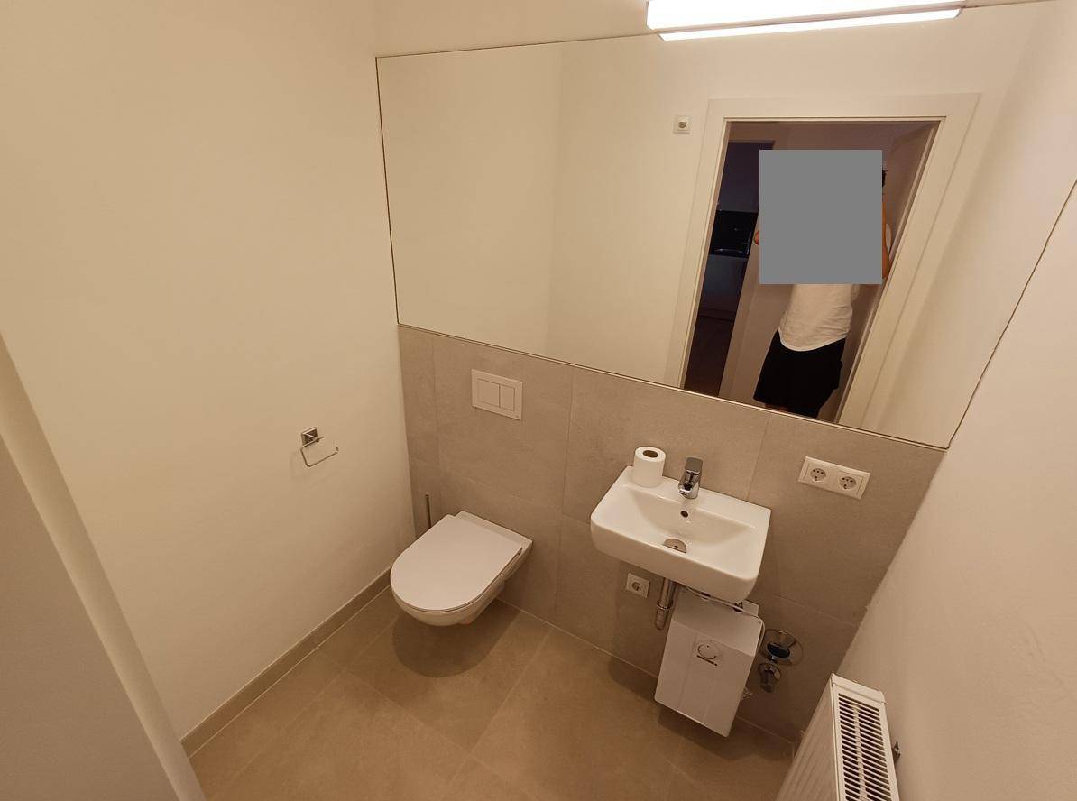 Modernes Gäste-WC mit wandhängender Toilette, kleinem Waschbecken und großem Spiegel, in hellen Farbtönen gehalten.