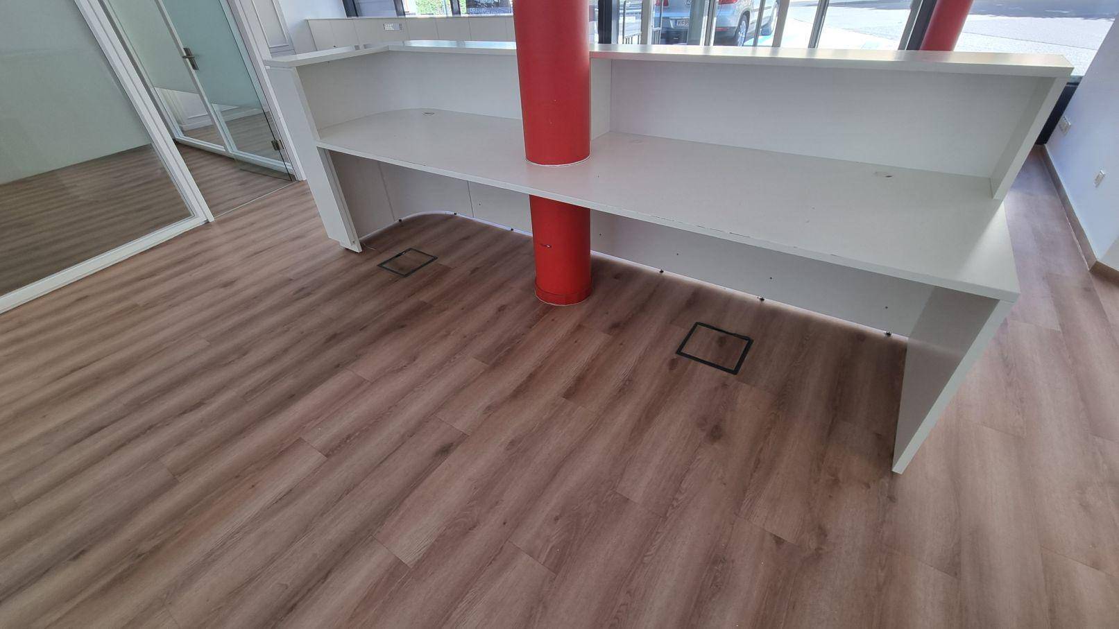 Moderner Empfangsbereich mit weißer Theke, Holzboden und einer auffälligen roten Säule.