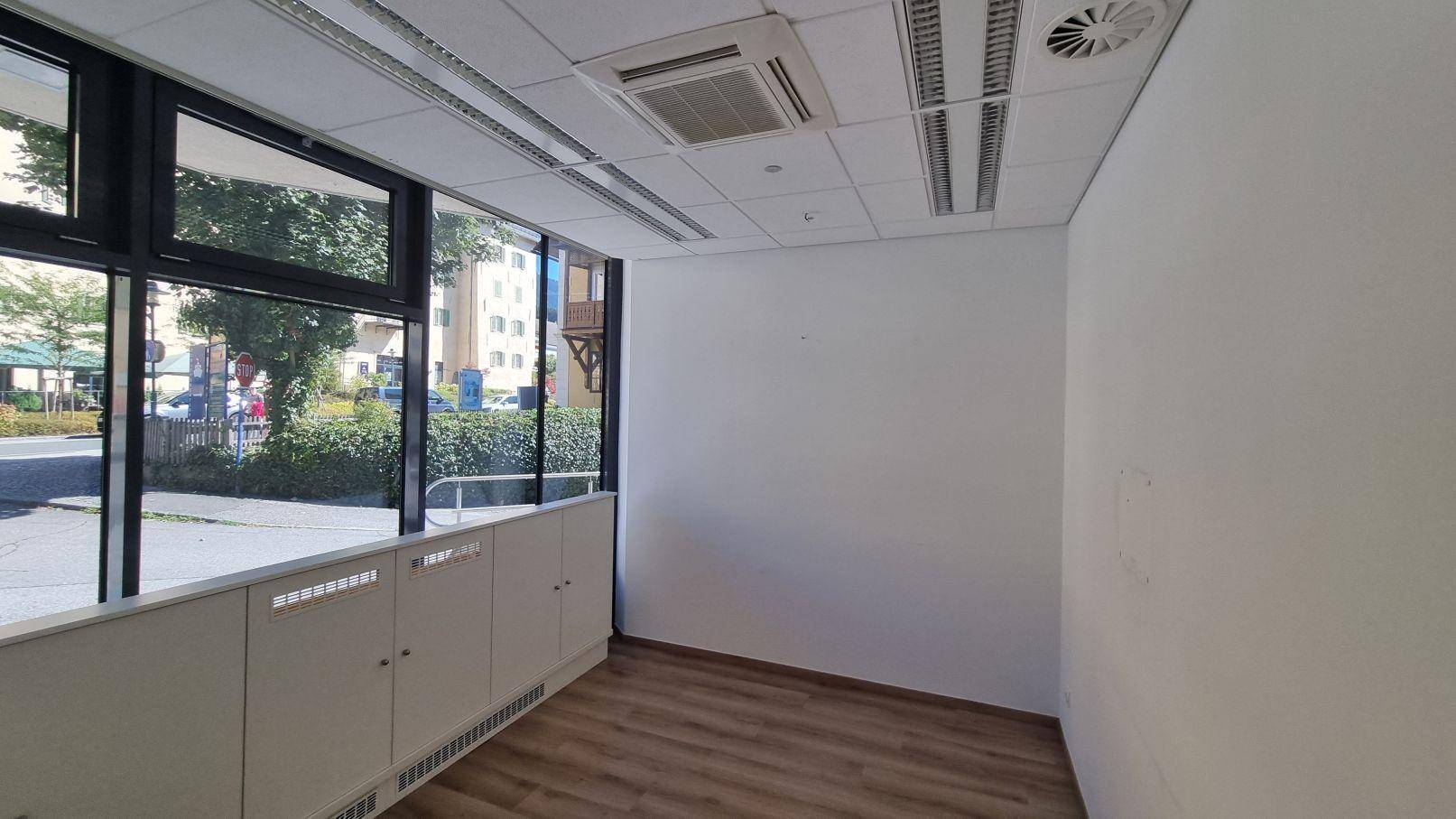 Heller Büroraum mit großen Fenstern, Holzboden und abgehängter Decke mit integrierter Beleuchtung.