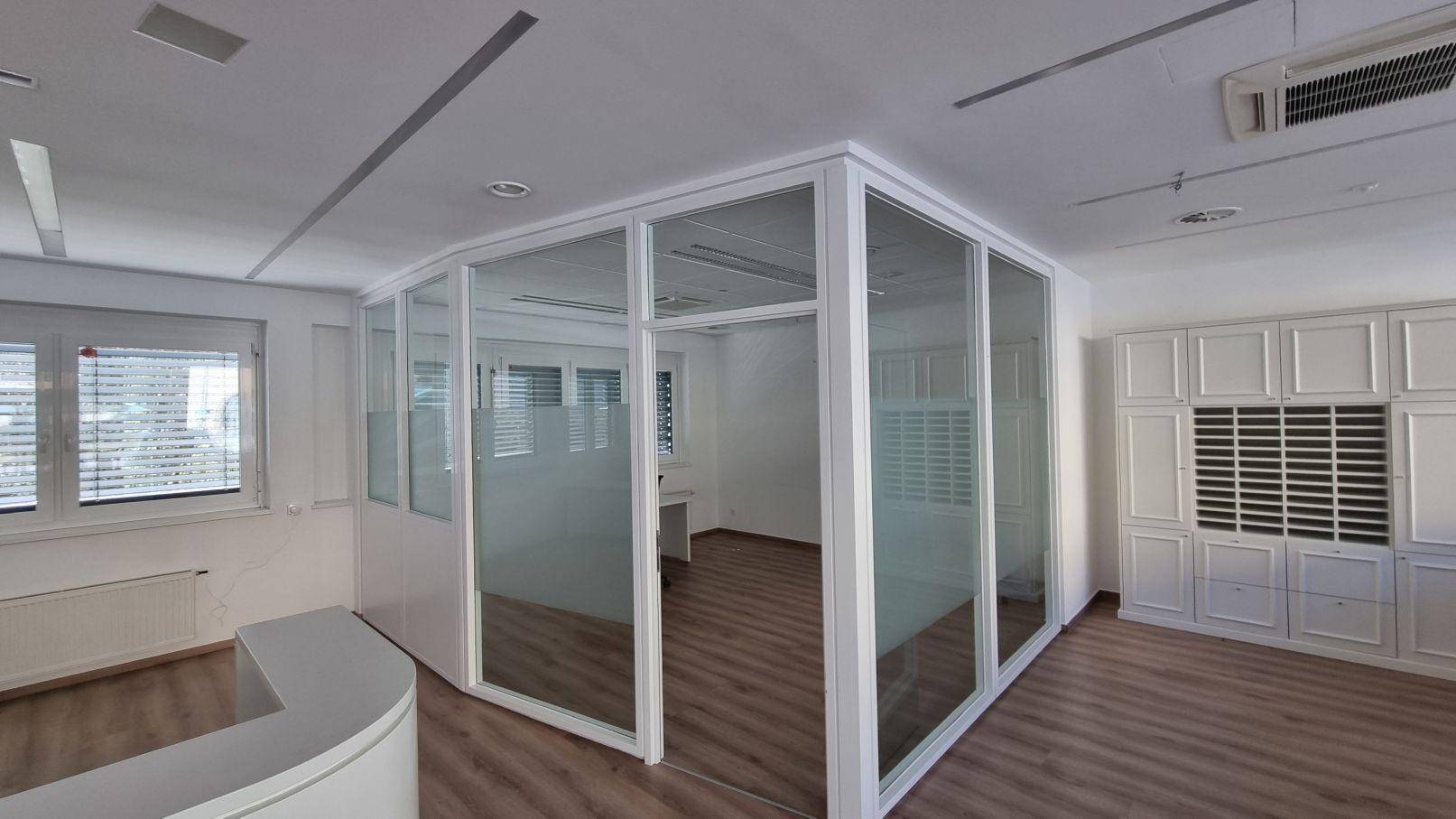 Moderner Büroraum mit Glaswänden, Holzboden und weißen Einbauschränken, ideal für flexible Arbeitsbereiche.
