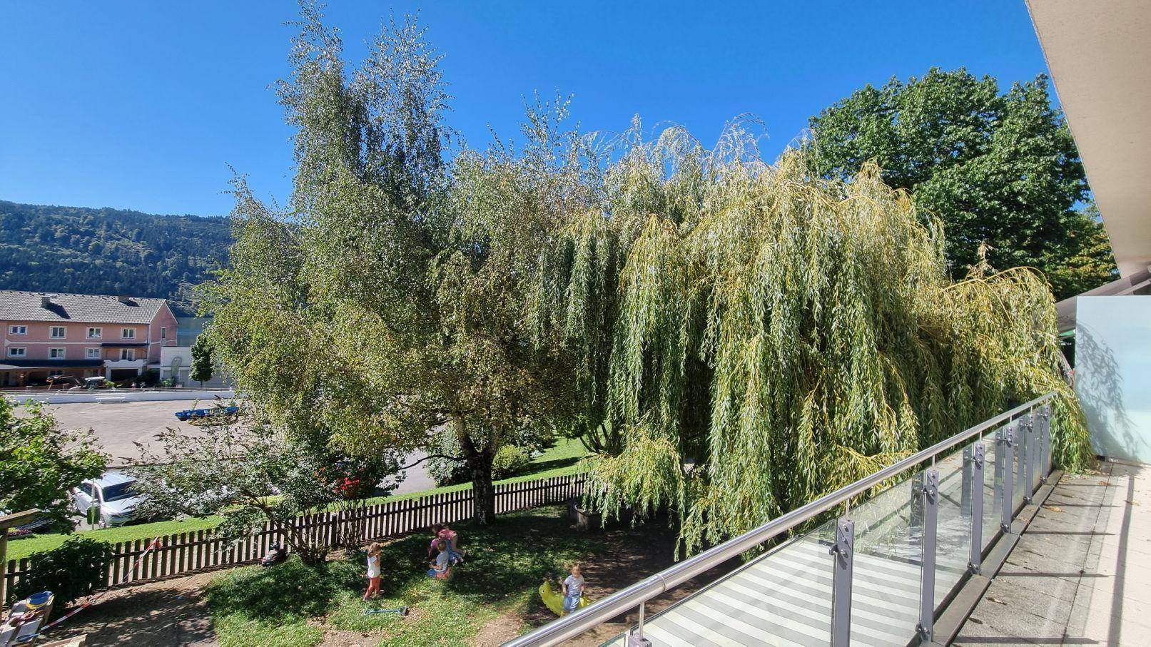 Balkon mit weitem Blick über einen Garten mit Bäumen und die umliegende Natur unter blauem Himmel.