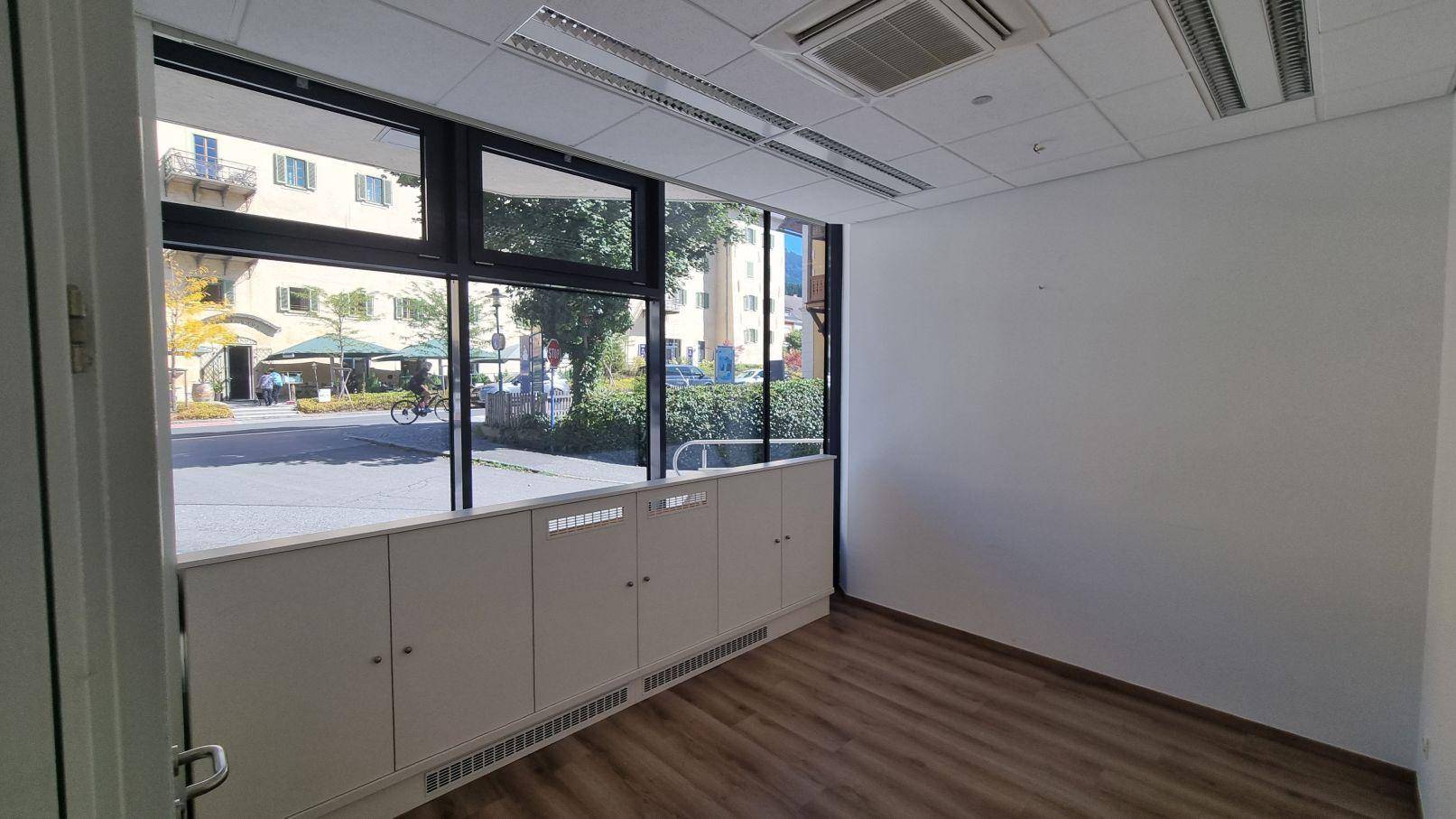 Heller Büroraum mit großen Fenstern, Holzboden und abgehängter Decke mit integrierter Beleuchtung.