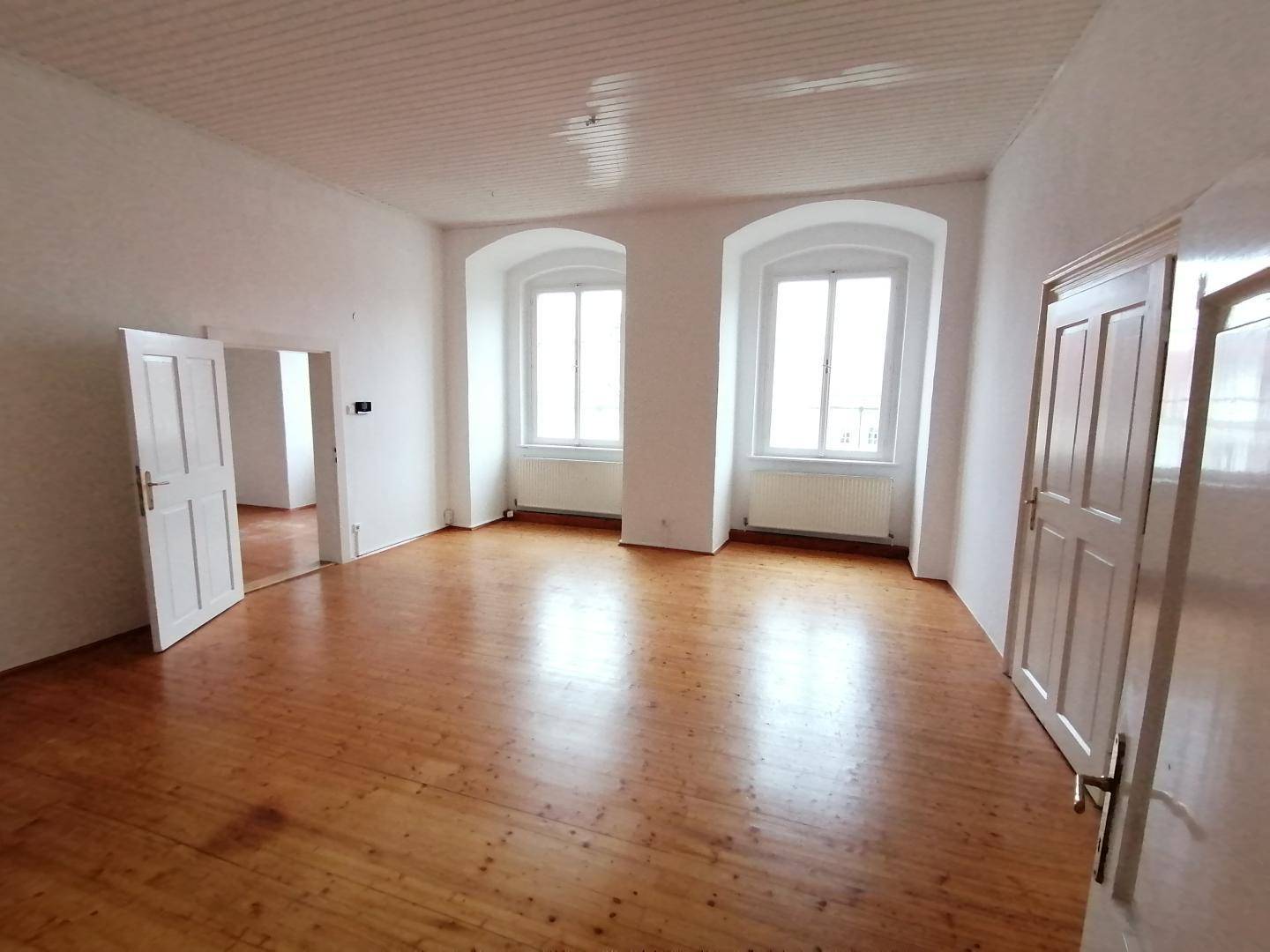 Helles, unmöbliertes Zimmer mit Holzdielenboden und zwei hohen Fenstern, bereit zur individuellen Gestaltung.