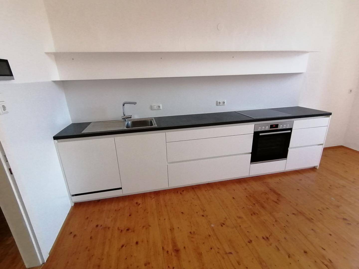 Moderne, minimalistische Küchenzeile mit weißen Schränken, dunkler Arbeitsplatte und integrierten Geräten.