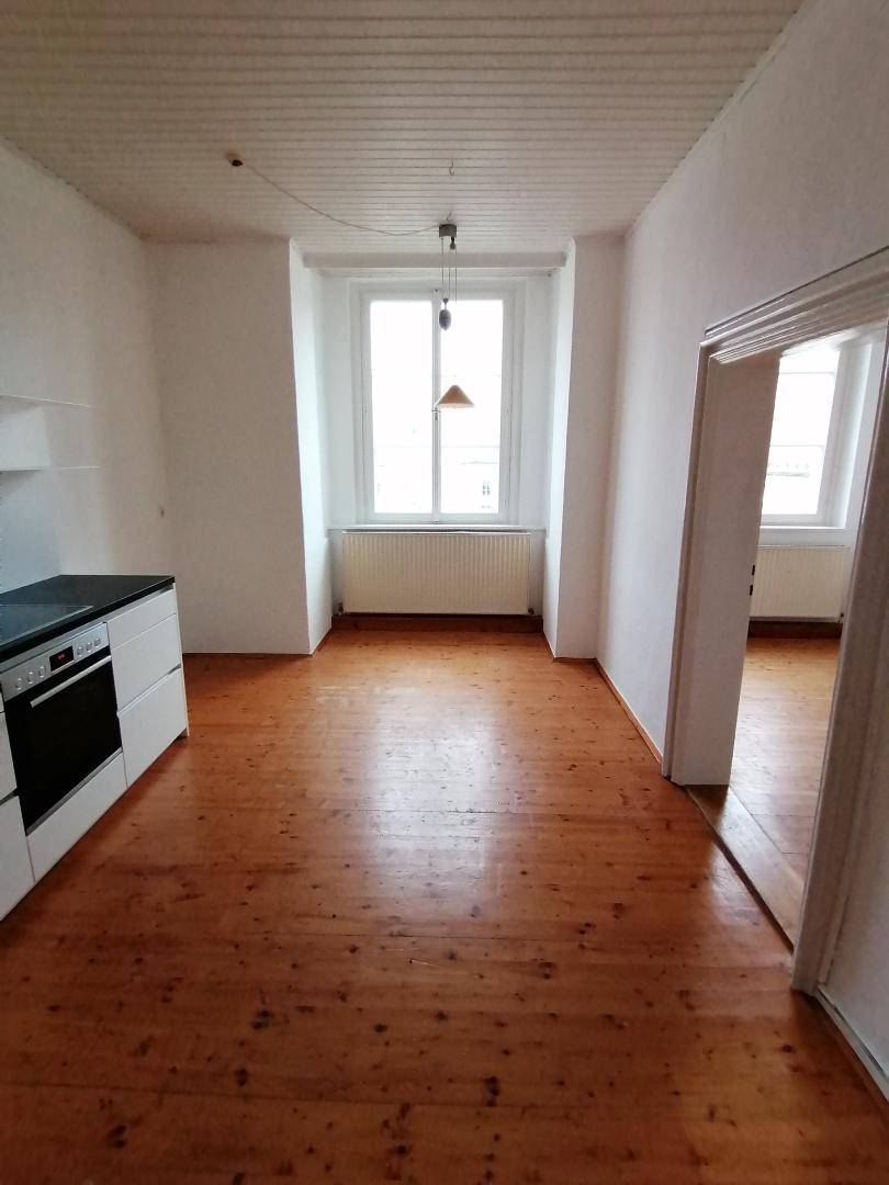 Einfache Küchenzeile in einem hellen Raum mit Holzdielenboden und einem großen Fenster.