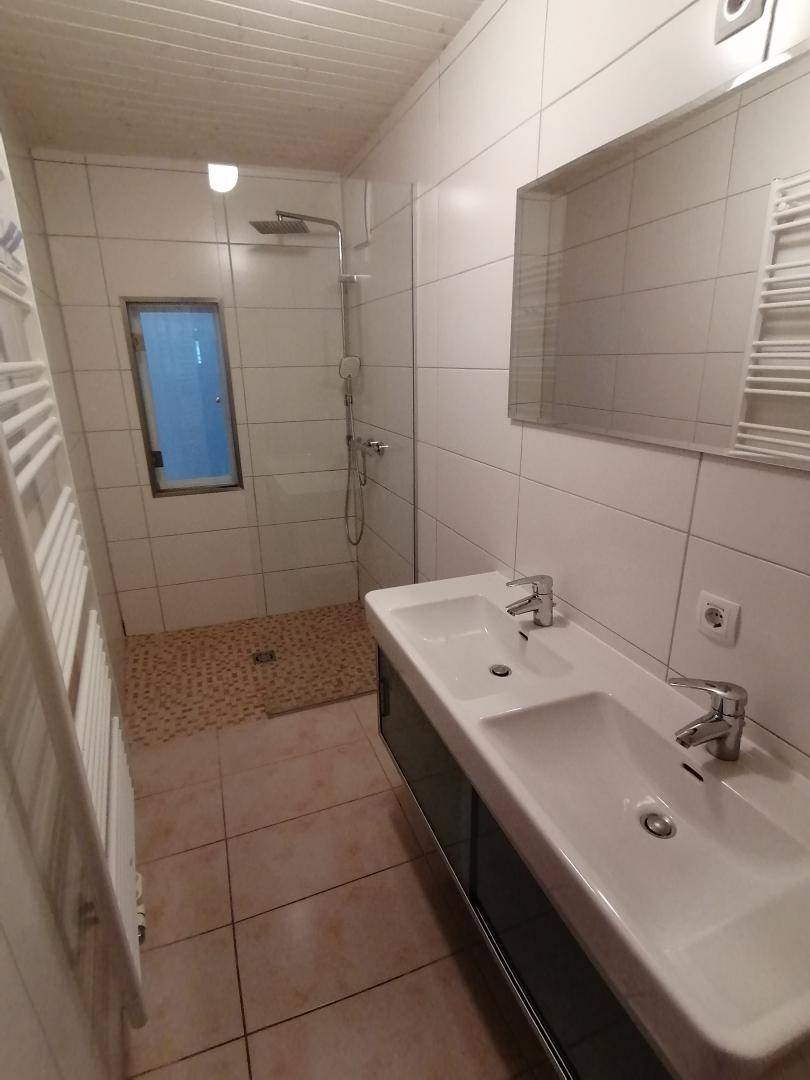 Modernes Badezimmer mit Doppelwaschbecken, begehbarer Dusche und hellen Fliesen.