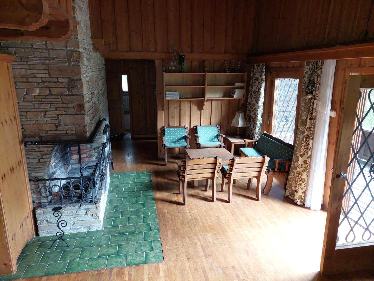 Gemütliches Wohnzimmer mit Holzwänden, Steinkamin und traditionellen Sitzmöbeln.