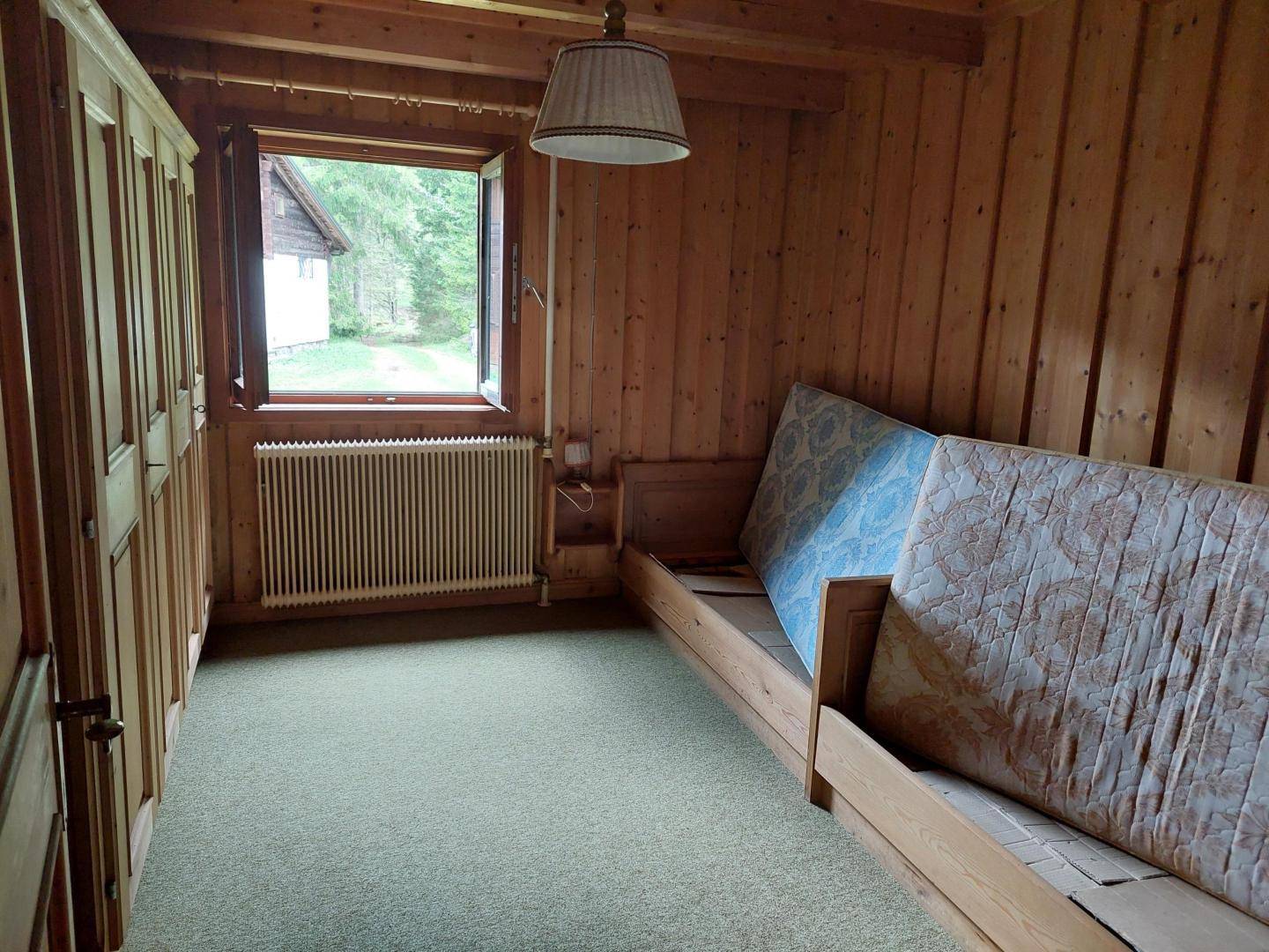 Rustikales Schlafzimmer mit Holztäfelung, Einzelbett, Kleiderschrank und Blick ins Grüne.