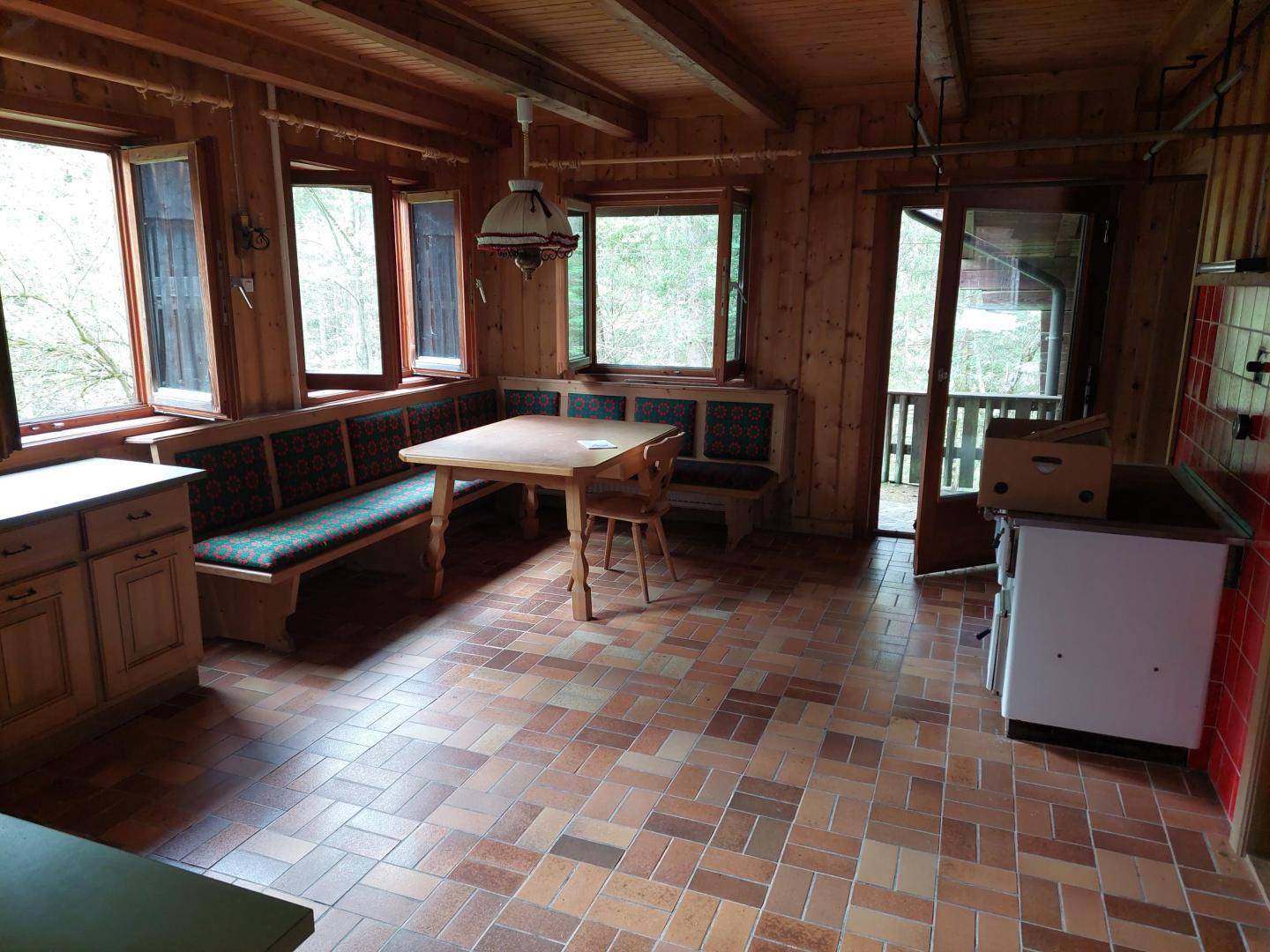 Gemütlicher Wohn-Essbereich mit Holztäfelung, Eckbank, Terrakotta-Fliesenboden und Zugang nach draußen.