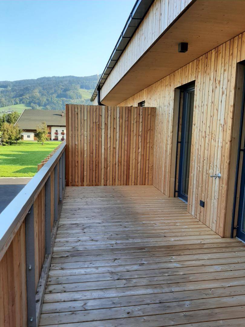 Geräumiger Holzbalkon mit Holzverkleidung und Blick auf die umliegende grüne Landschaft.