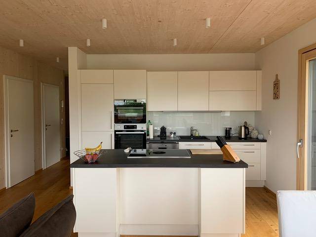 Moderne Einbauküche mit weißen Schränken, dunkler Arbeitsplatte und einer Kücheninsel in einem hellen Raum.