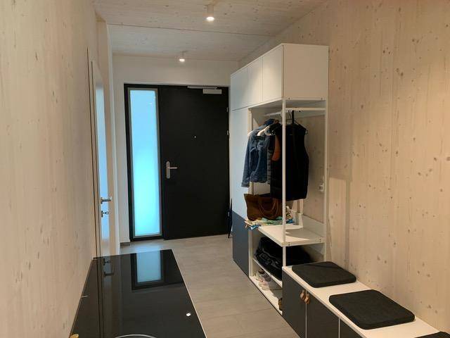 Heller Eingangsbereich mit moderner Garderobe, Fliesenboden und einer dunklen Eingangstür.