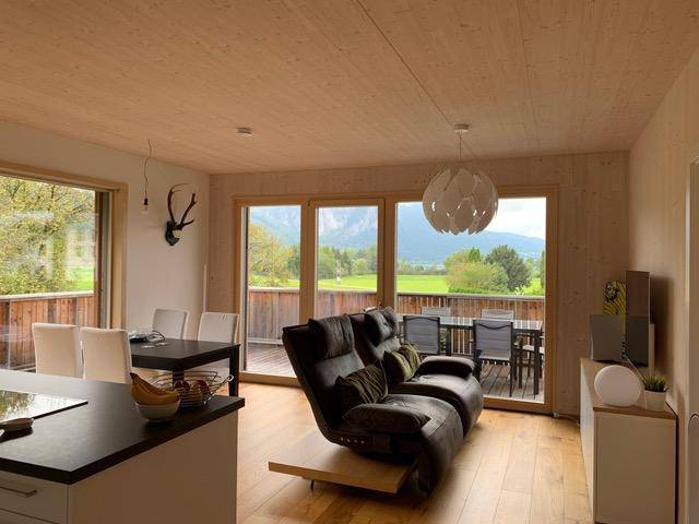 Offener Wohn-Essbereich mit Holzboden und -decke, gemütlichem Sofa und Zugang zu einem Balkon mit Bergblick.