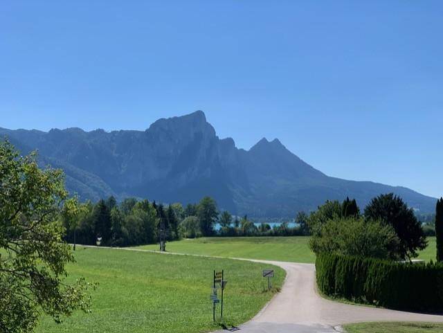 Malerische Landschaft mit majestätischen Bergen, einem ruhigen See und weiten grünen Feldern unter blauem Himmel.