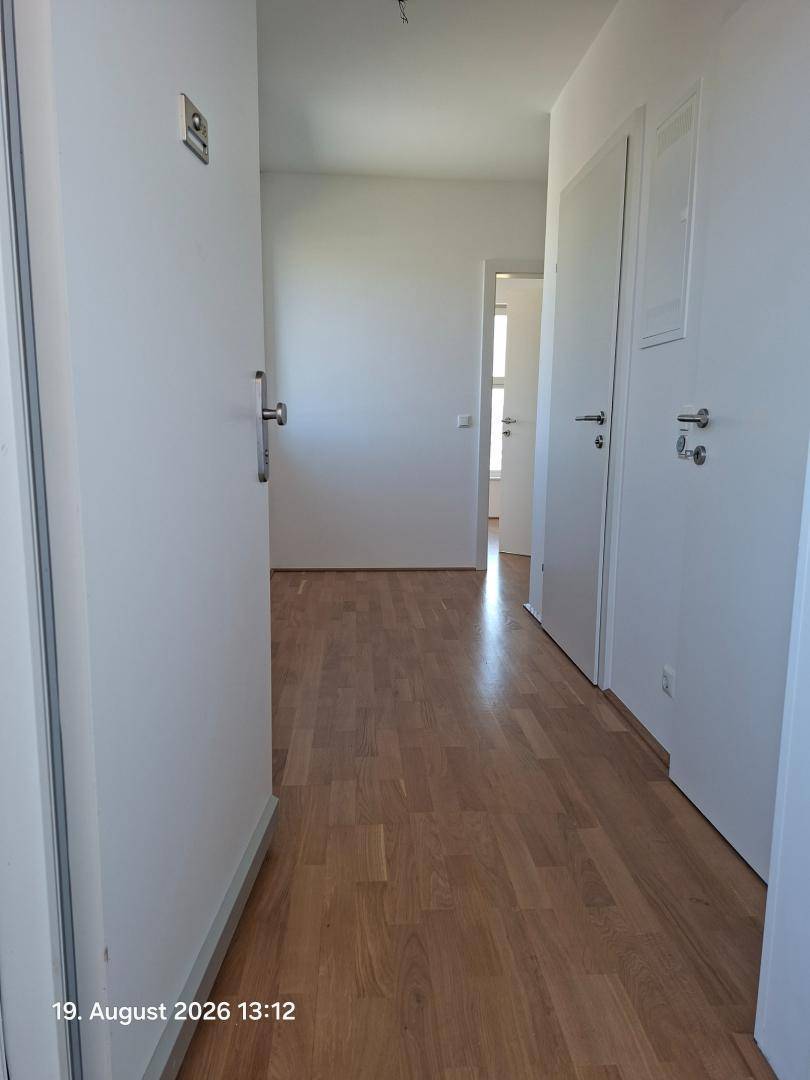 Heller Flur mit Holzparkettboden und weißen Wänden, der zu weiteren Räumen führt.