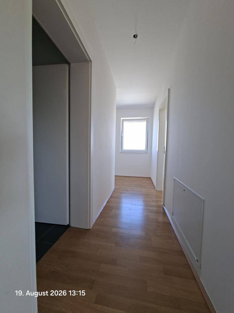 Heller Flur mit Holzparkettboden und einem Fenster am Ende, das Tageslicht hereinlässt.