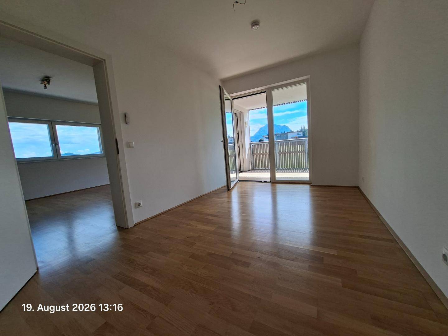 Heller Wohnraum mit Holzparkettboden und direktem Zugang zu einem Balkon mit Aussicht.