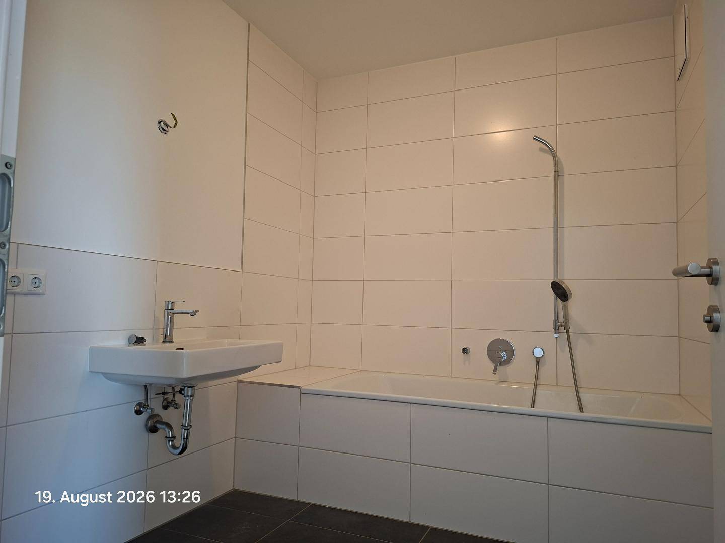 Modernes Badezimmer mit Badewanne, weiß gefliesten Wänden und dunklem Boden.