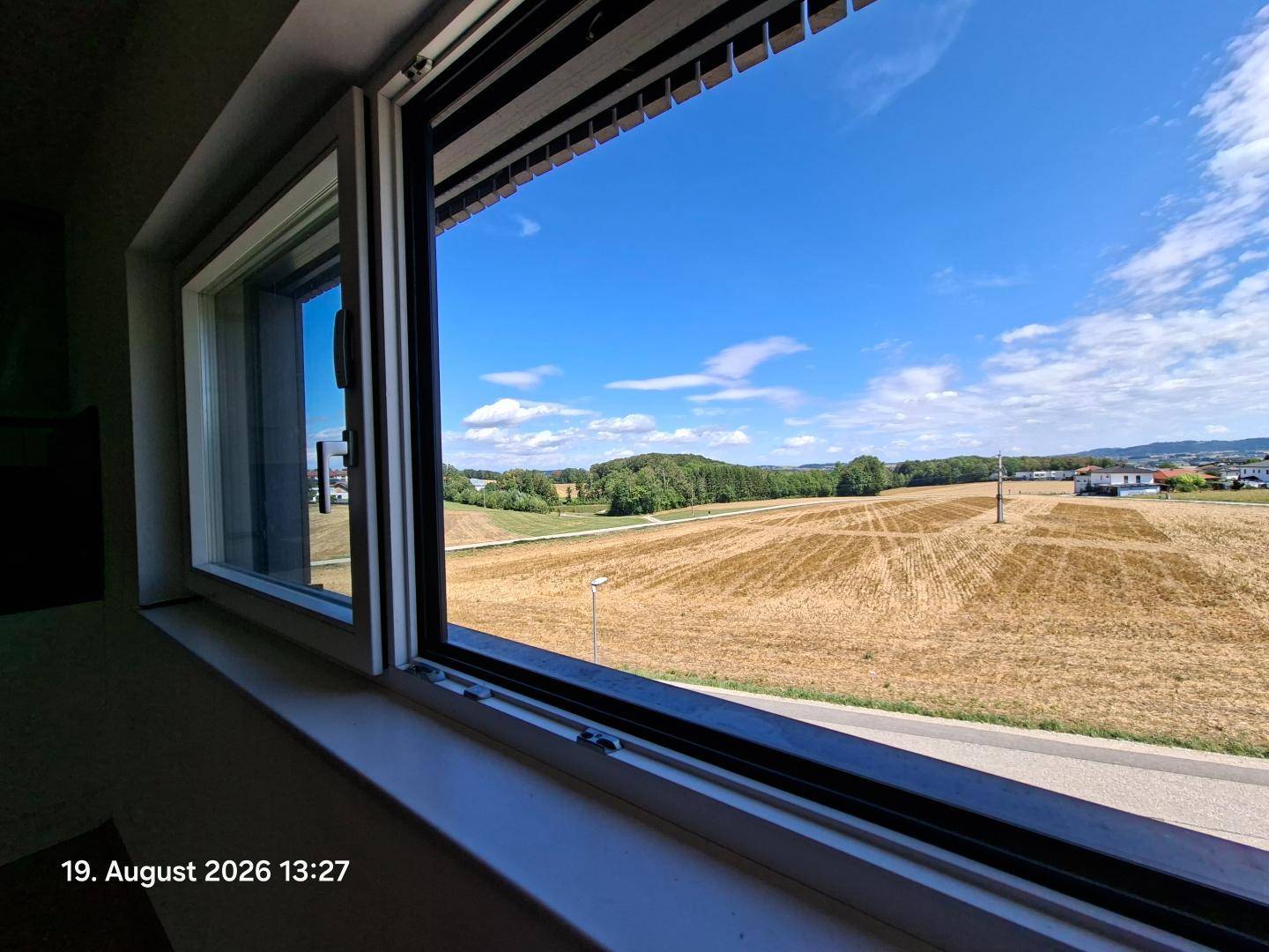Weitläufiger Blick aus dem Fenster auf Felder und die umliegende Landschaft unter blauem Himmel.