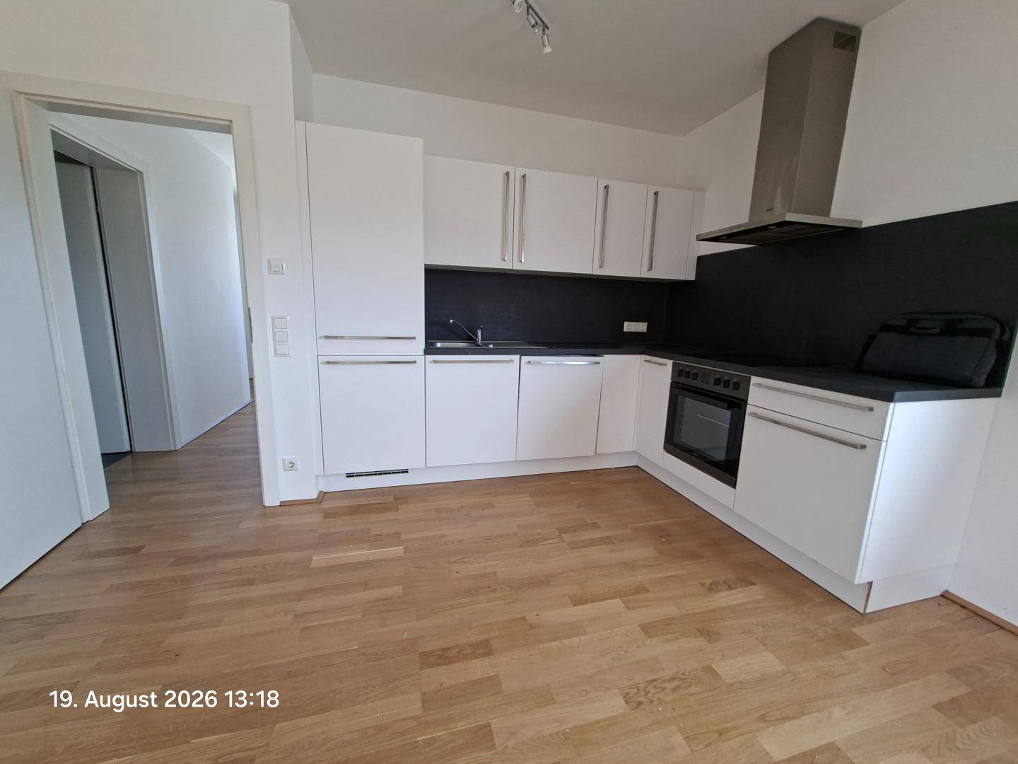 Moderne Einbauküche mit weißen Schränken, schwarzen Arbeitsplatten und Holzparkettboden.
