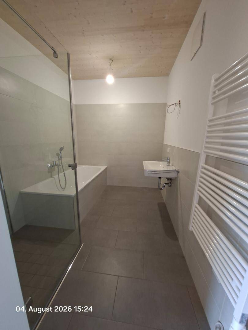 Helles Badezimmer mit Badewanne, Dusche und beheiztem Handtuchhalter in modernem Design.