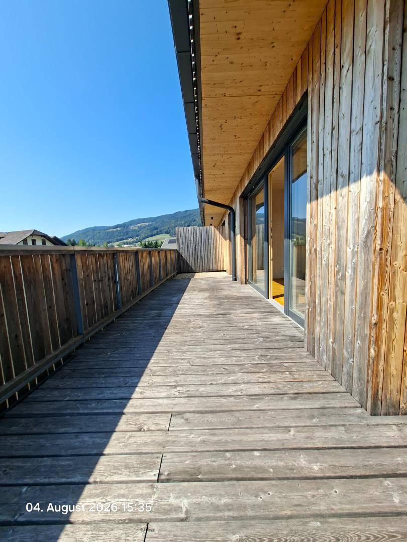 Langer Holzbalkon mit Holzgeländer und Blick auf die umliegende grüne Landschaft.