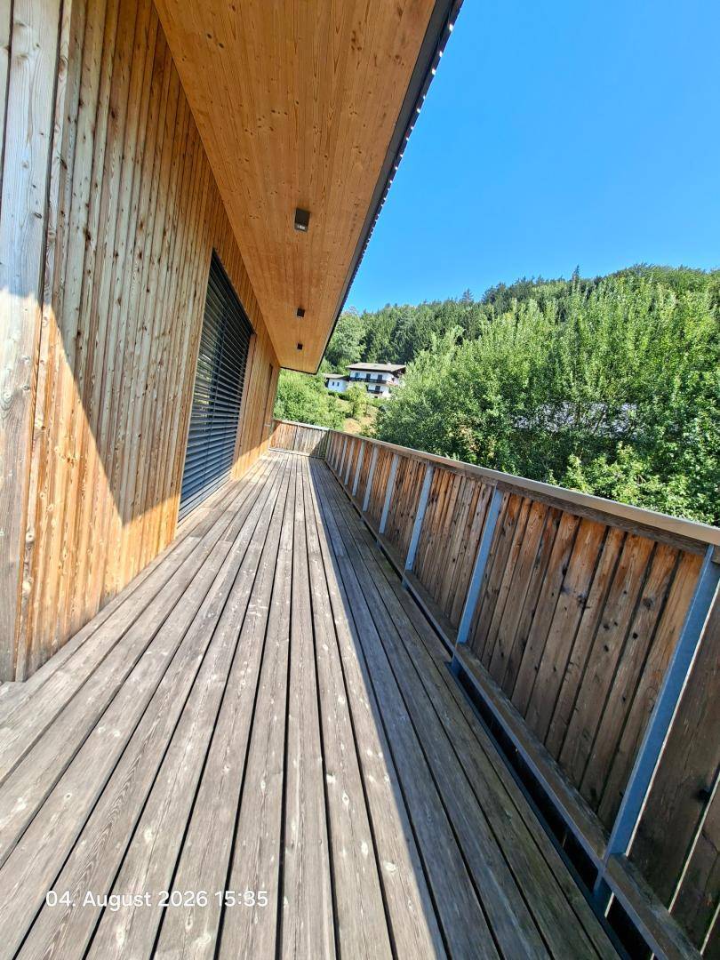 Geräumiger Holzbalkon mit Holzverkleidung und Blick auf bewaldete Hügel und Natur.