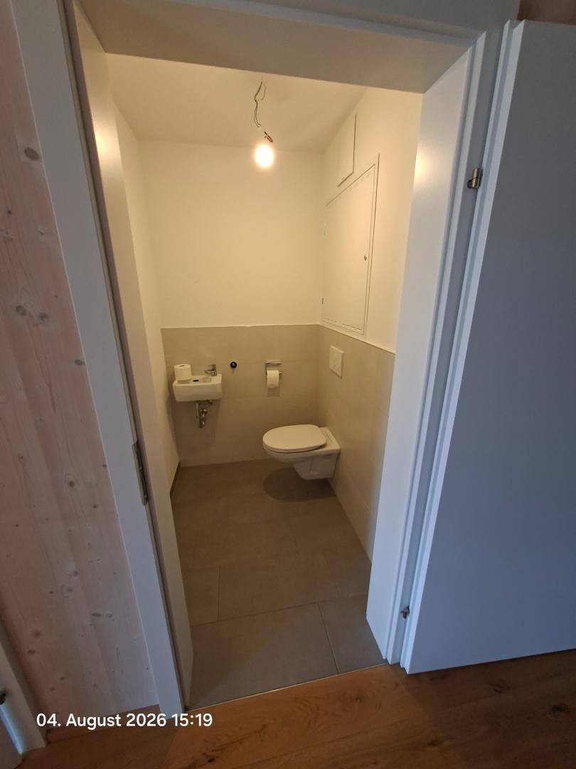 Kleines Gäste-WC mit Wand-WC, Waschbecken und hellen Fliesen.