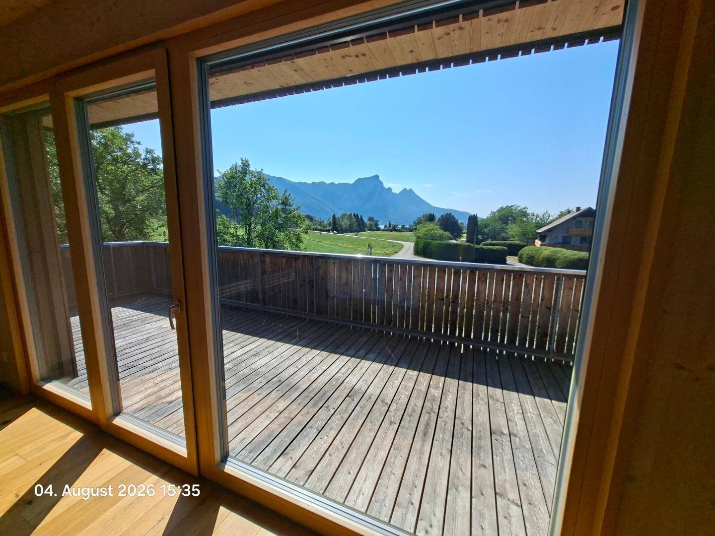 Heller Innenraum mit Holzboden und Zugang zu einem großen Holzbalkon mit Bergblick.