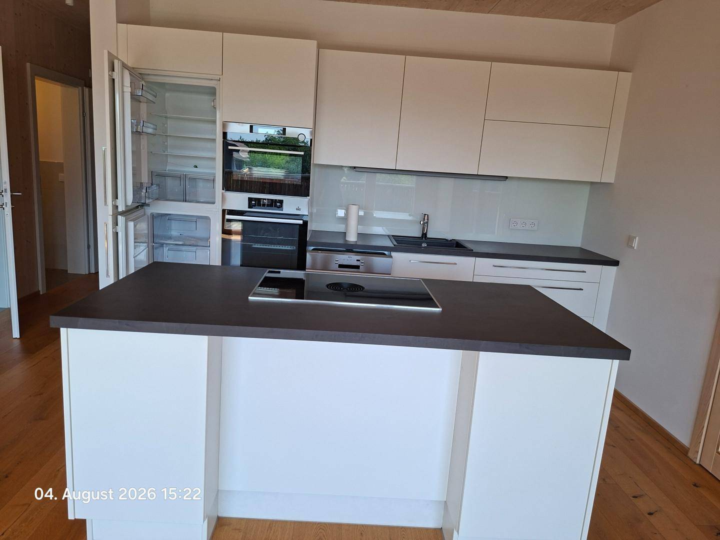 Moderne Einbauküche mit weißen Schränken, dunkler Arbeitsplatte und integrierten Geräten.
