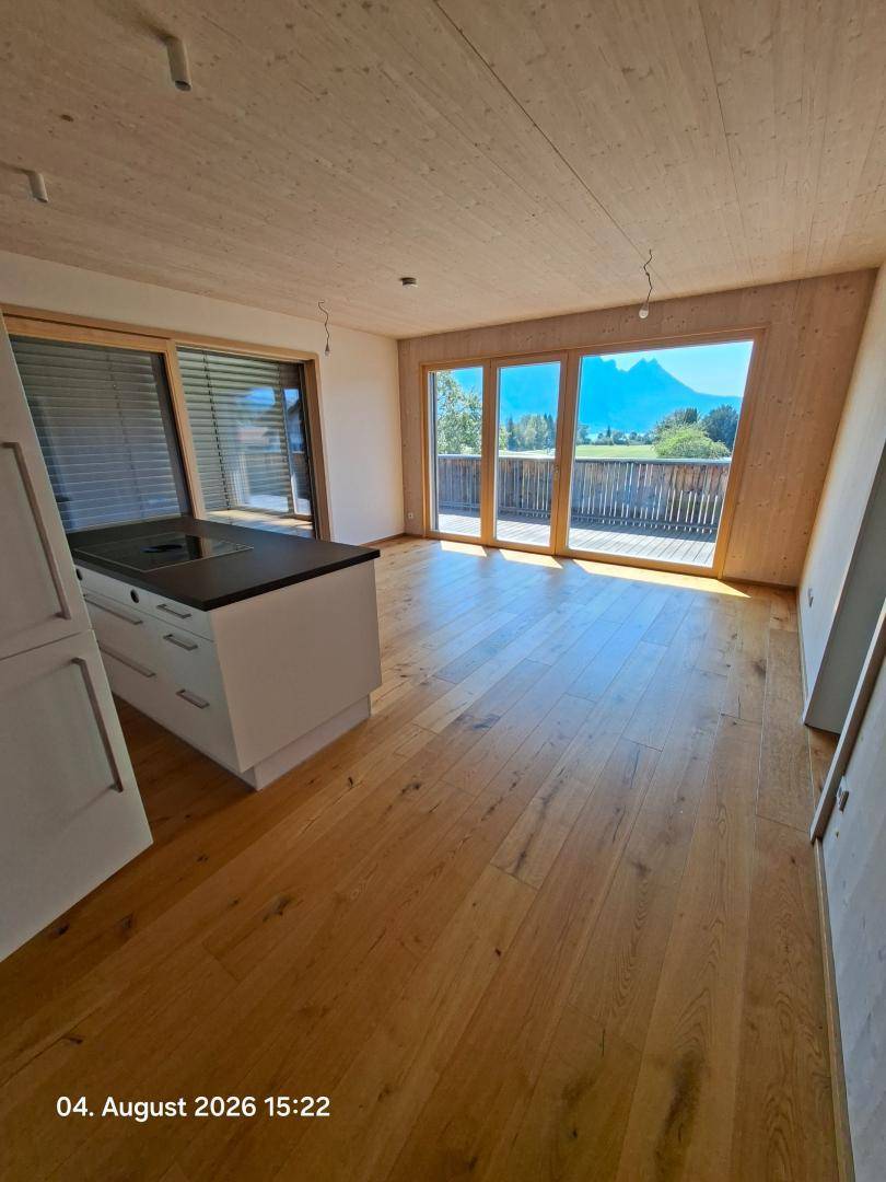 Offener Wohnbereich mit Holzboden, Kücheninsel und großen Fenstern mit Bergblick.