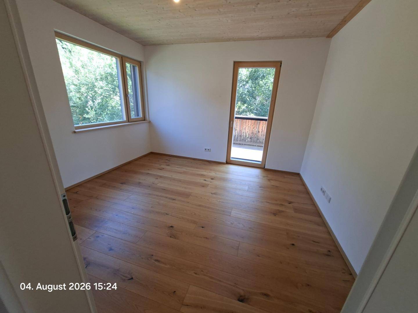 Helles Schlafzimmer mit Holzboden und Fenster mit Blick auf die grüne Umgebung.