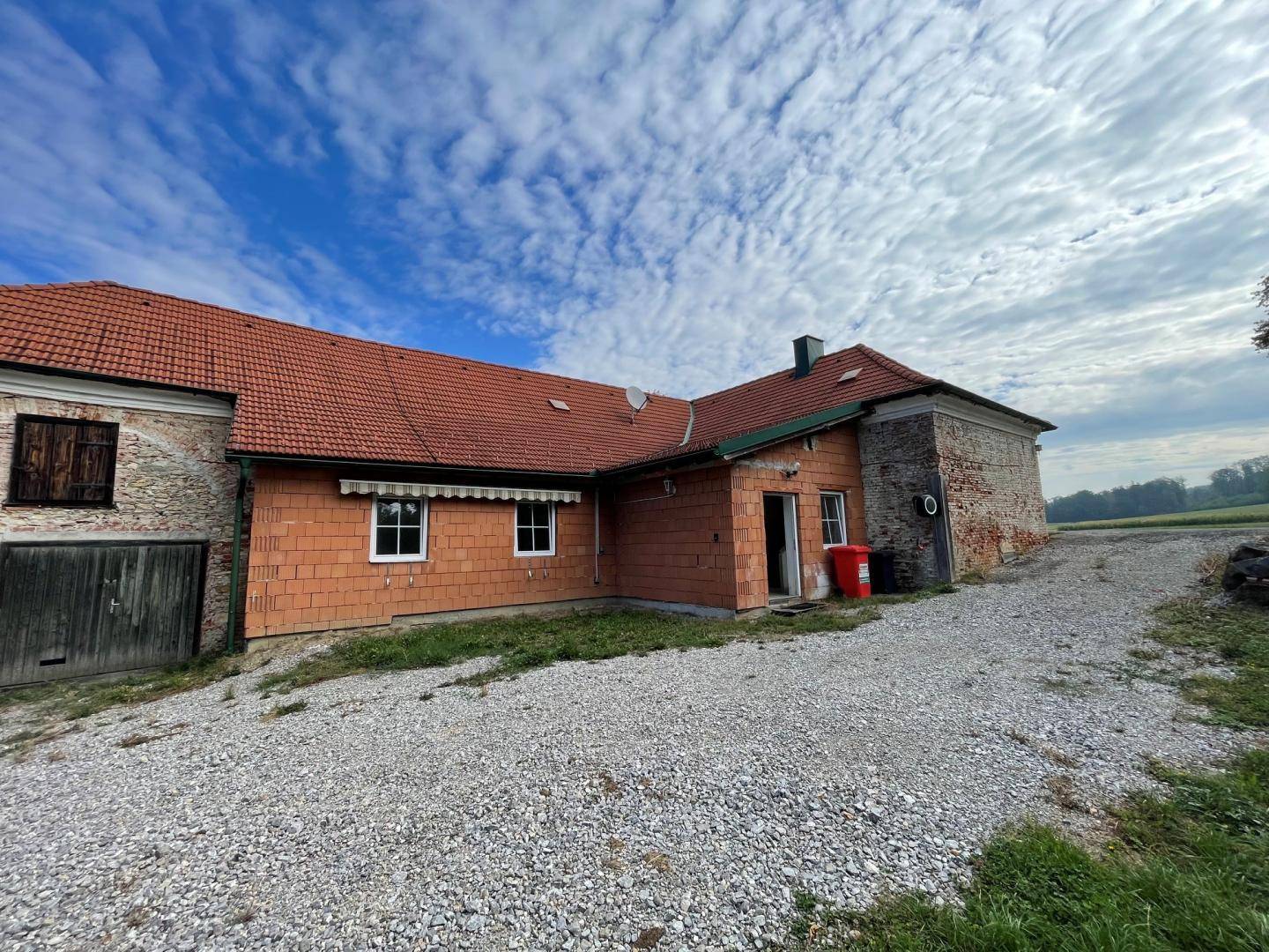 Rückseite des Gebäudes mit Anbau, teilweise verputzter Fassade und Schotterfläche.