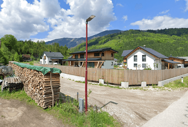 Moderne Häuser mit Holzfassaden und Gärten in einer ländlichen Umgebung mit Bergen im Hintergrund.