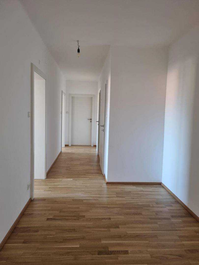 Heller Flur mit Holzfußboden und weißen Wänden, der zu weiteren Räumen führt.