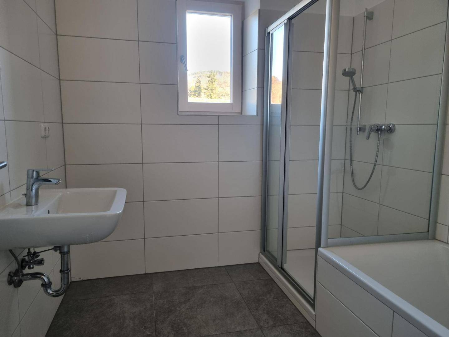 Funktionales Badezimmer mit Waschbecken, Duschkabine, Badewanne und Fenster.