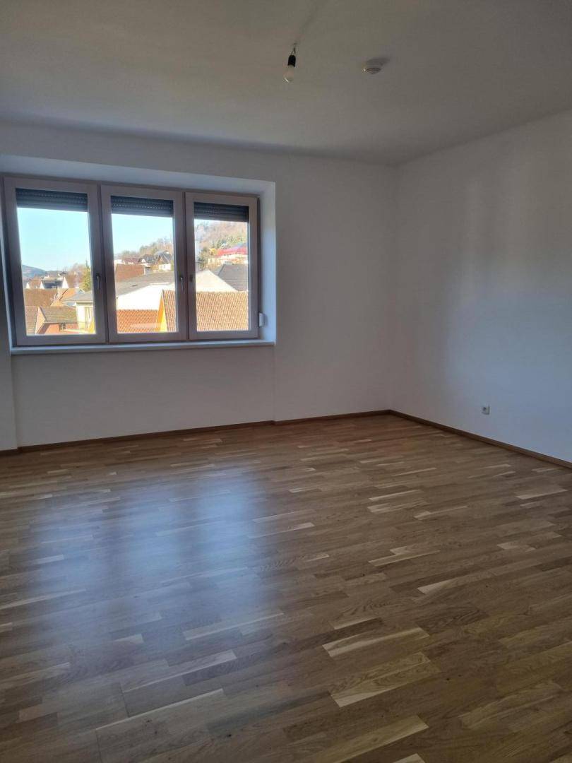 Leeres Zimmer mit hellem Holzfußboden und einem Fenster mit Blick ins Grüne.
