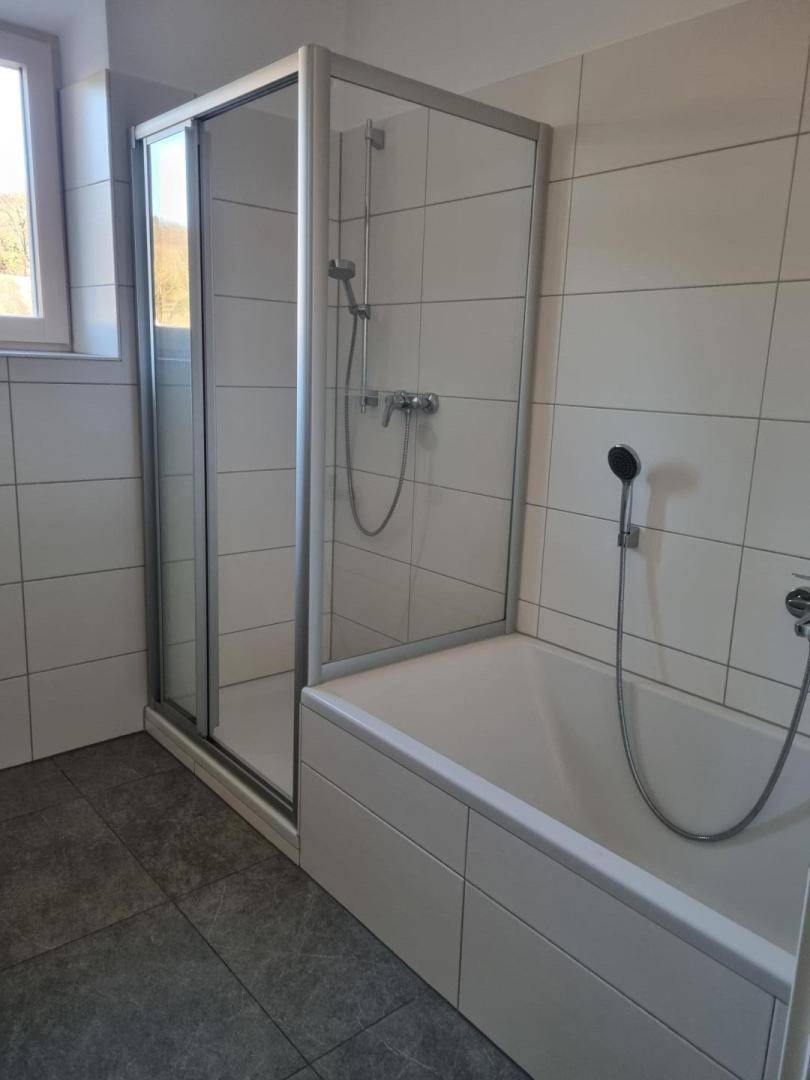 Helles Badezimmer mit weißen Fliesen, einer Duschkabine und einer Badewanne.