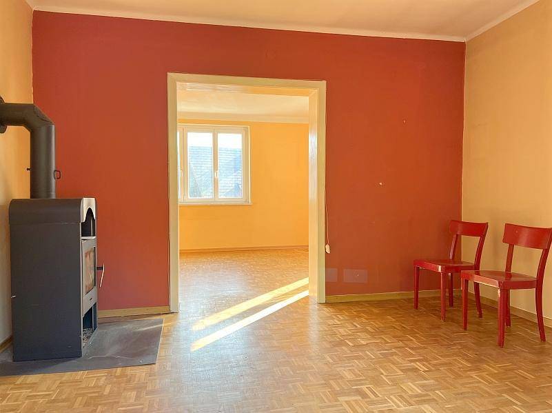 Gemütlicher Wohnbereich mit Holzofen, Parkettboden und einer roten Akzentwand.