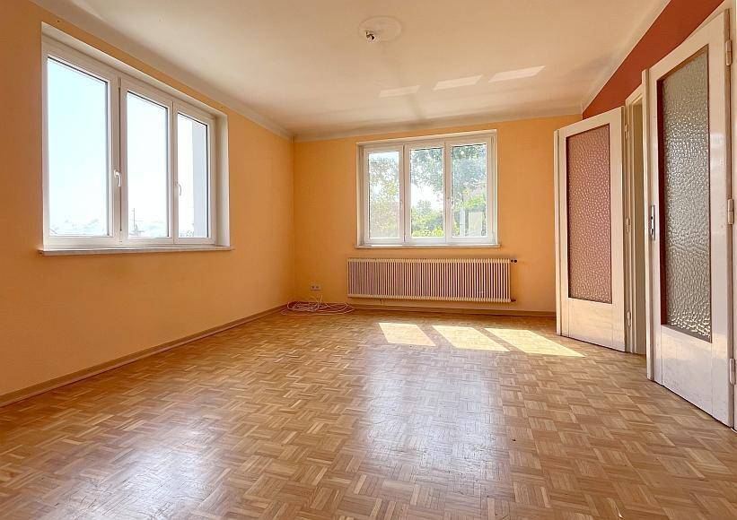Heller Wohnraum mit Fischgrätparkettboden, orangefarbenen Wänden und zwei großen Fenstern.