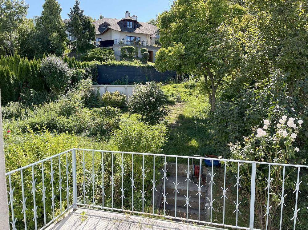 Blick von einem Balkon auf einen weitläufigen, grünen Garten mit terrassiertem Gelände und einem Haus im Hintergrund.