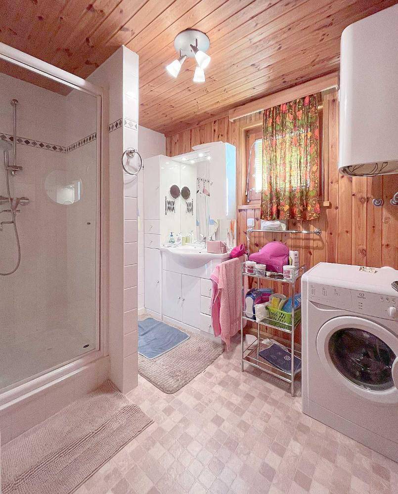 Badezimmer mit Dusche, Waschmaschine und Holzvertäfelung an den Wänden.