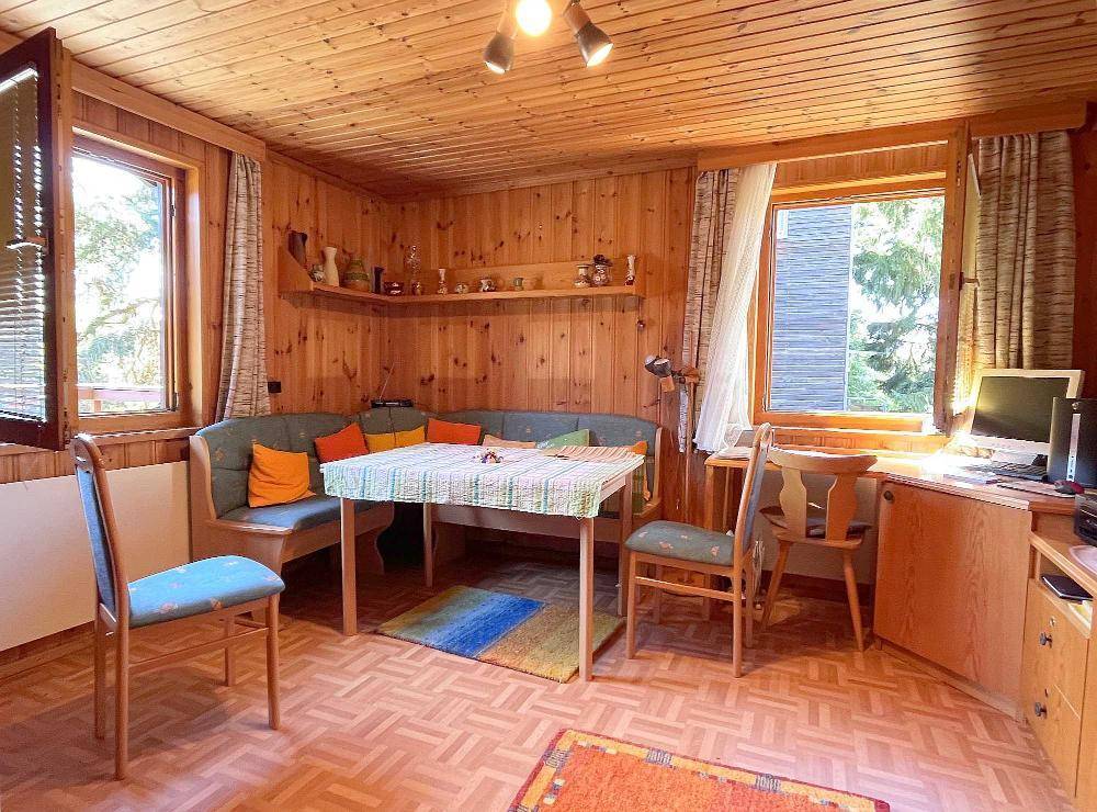 Rustikales Wohnzimmer mit Holzvertäfelung, Sitzecke und Arbeitsbereich am Fenster.