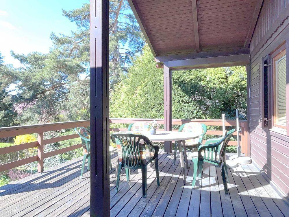 Überdachte Holzterrasse mit Sitzgelegenheiten und Blick auf den Garten und die Bäume.