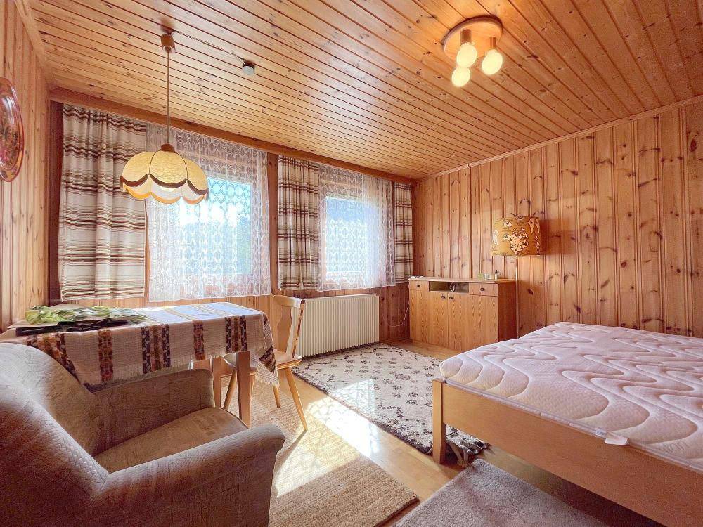 Helles Schlafzimmer mit Holzvertäfelung, Bett und gemütlichem Sessel am Fenster.