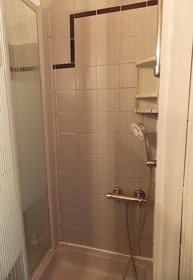 Einfache Duschkabine mit Fliesen und Handbrause in einem kompakten Badezimmer.