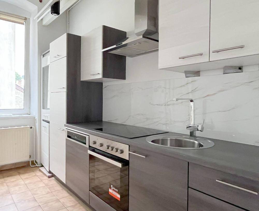 Funktionale Küche mit modernen Geräten, Spülbecken und Fenster für Tageslicht und Grünblick.