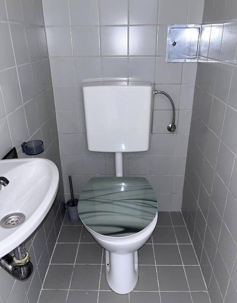 Kleines WC mit grauen Fliesen, einer Toilette und einem Waschbecken.